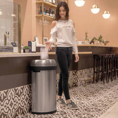 60L semi-round open bin - brushed stainless steel - lifestyle woman in cafe throwing rubbish away